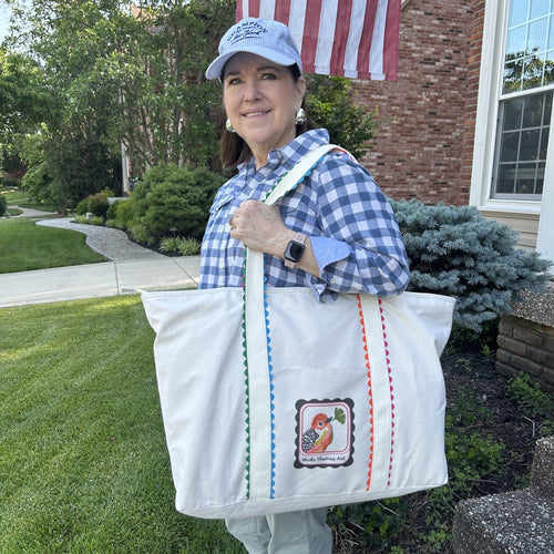 Woman holding a white mahjong tote bag with a logo, standing outdoors.