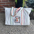 White  mahjong tote bag with colorful trim and a logo on a concrete surface.
