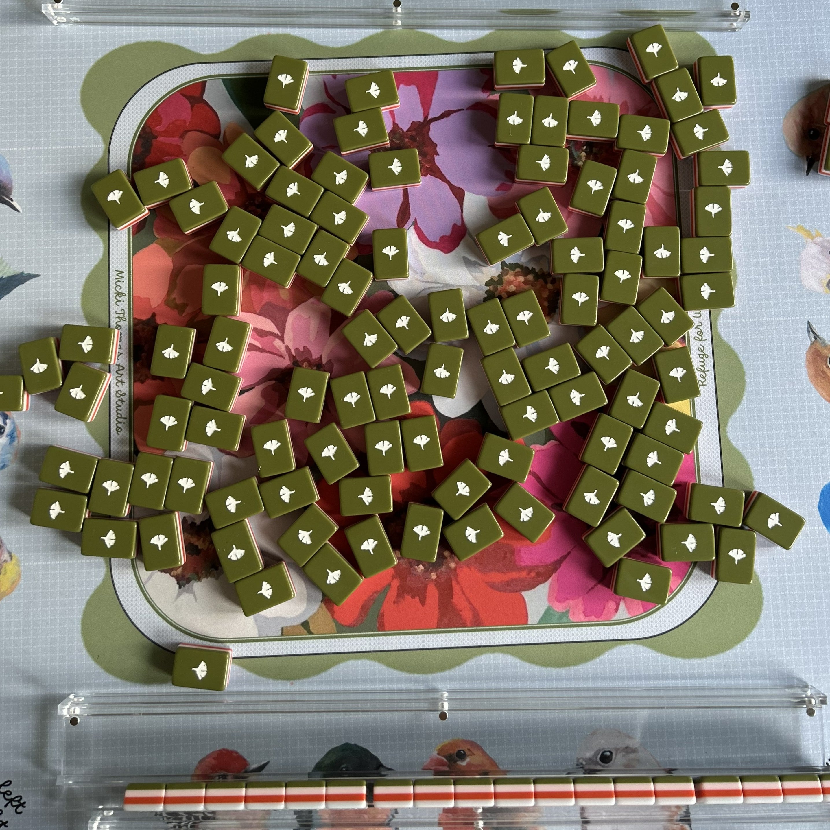 Green mahjong tiles with white ginko leaf symbols on a floral-patterned board