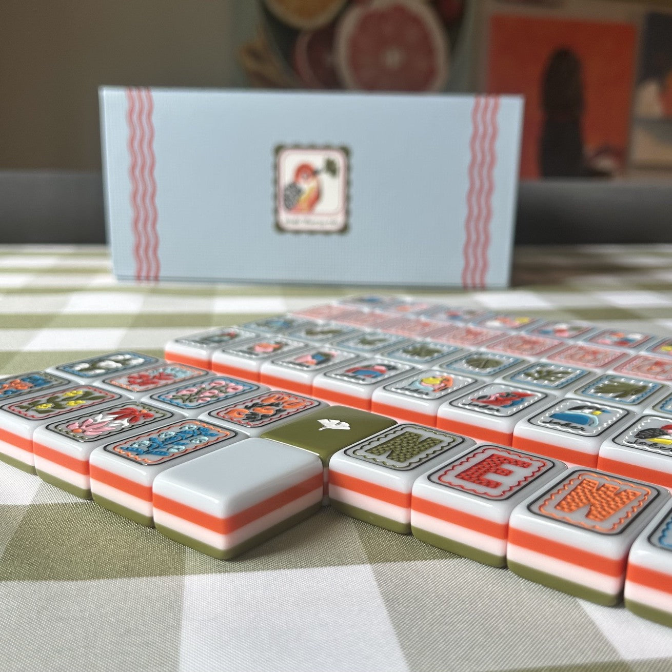 Set of Mahjong tiles on a checkered tablecloth with a box in the background